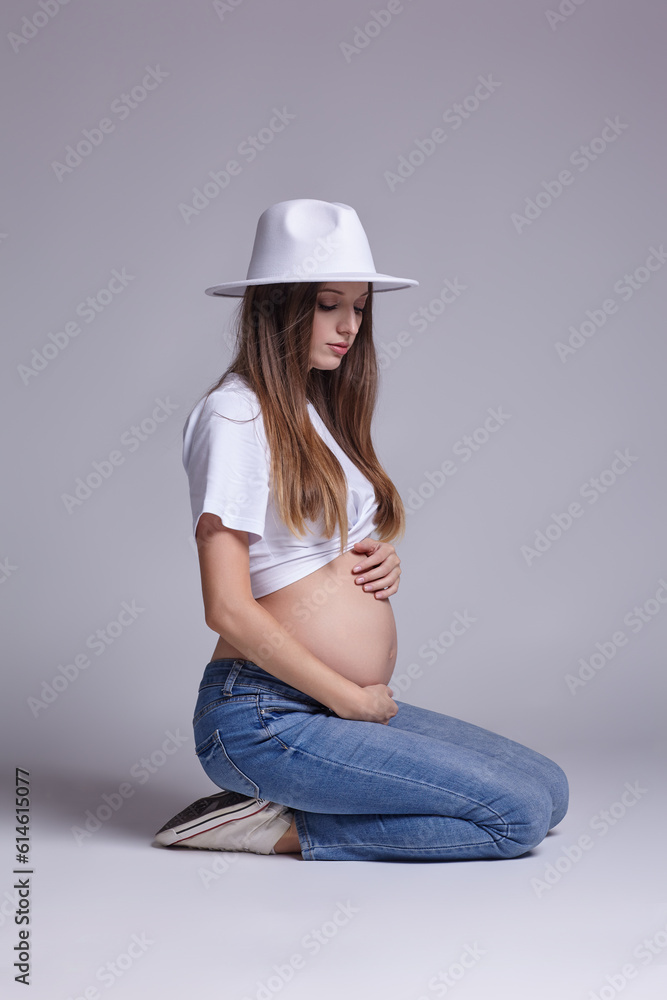 Young pretty pregnant woman in white tshirt, hat and jeans sit on the