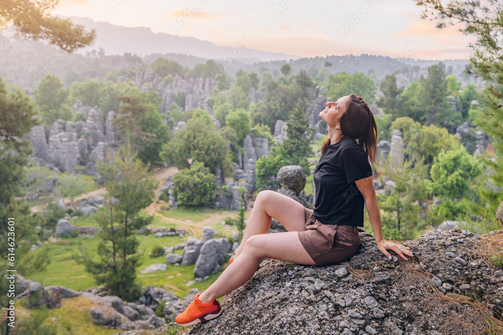 Obraz premium Happy traveler girl sitting on the rock cliff with view of stone remnants in Altinkaya, Turkey. Tourist attractions and destinations