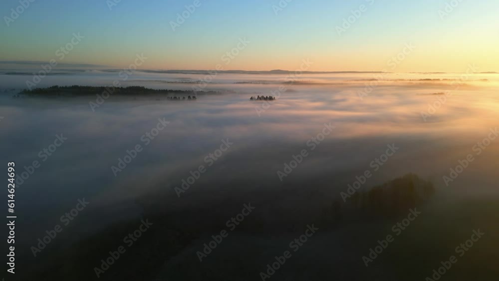 An aerial view of a landscape shrouded in fog with the orange hue of the rising sun An aerial view of a landscape shrouded in fog with the orange hue of the rising sun
