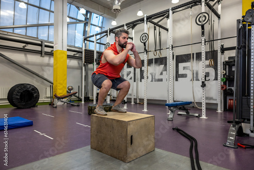 Bearded man having workout, jumping up on wooden box in crossfit gym.