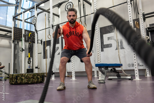Strong powerful man working out with battle ropes at gym, developing strenth and endurance. photo