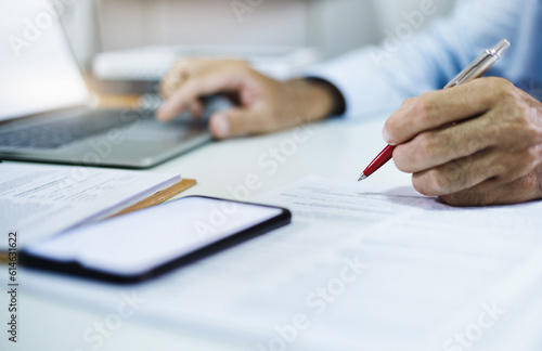 Businessman investor checking financial report or business contract from documents lying on his desk, A man working or meeting online with computer laptop on desk at home, Select focus at pen in hand