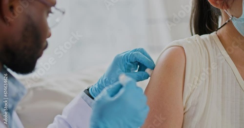 Young african american male doctor injecting flu or corona virus vaccine for female patient in a health clinic. Medical nurse use hypodermic needle and a syringe put shot of drug for treatment.