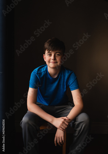 Portrait of smiling tween boy sitting on a chair in dark room.