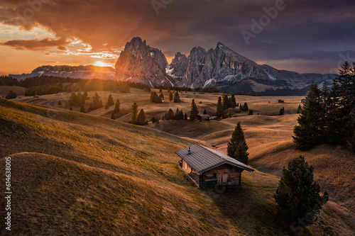 Alpe di Siusi, Italy - Golden autumn sunrise with a wooden chalet at Seiser Alm in South Tyrol province in the Dolomites mountain range with Saslonch (Sassolungo or Langkofel) mountain at background photo
