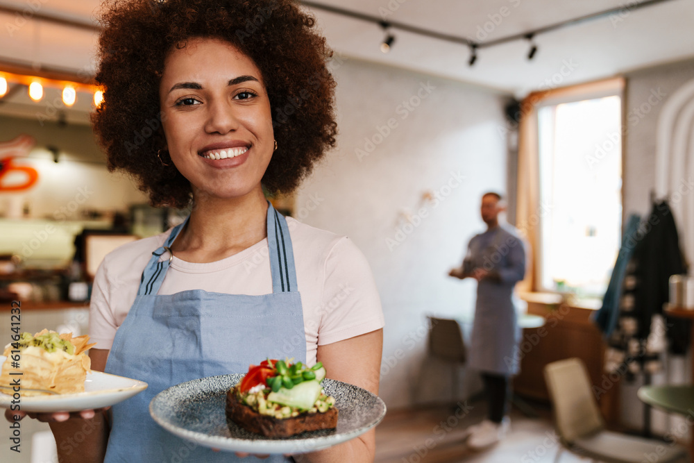 Cheerful waitress carrying plates with meal while working in cafe