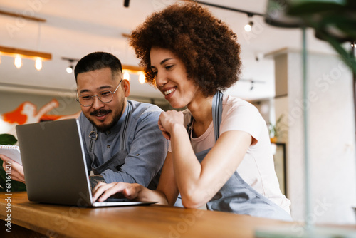 Two smiling business owners using laptop while working in cafe