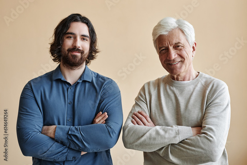 Waist up portrait of adult father and son looking at camera against wall