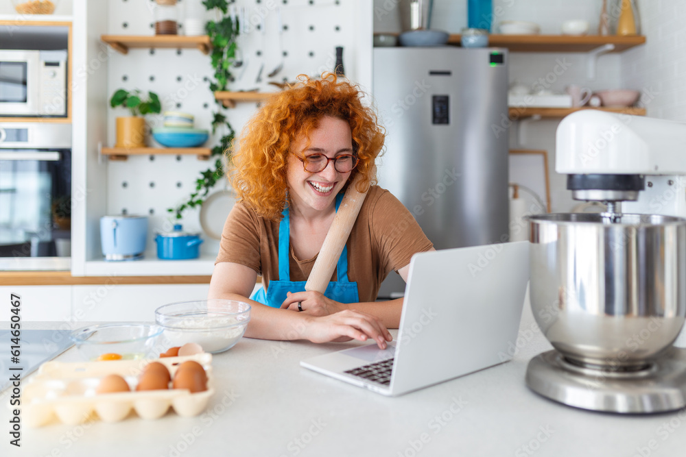 A young woman learns to cook, she watches video recipes on a laptop in the kitchen and cook a dish . Cooking at home concept A young woman learns to cook, she watches video recipes on a laptop in the kitchen and cook a dish . Cooking at home concept