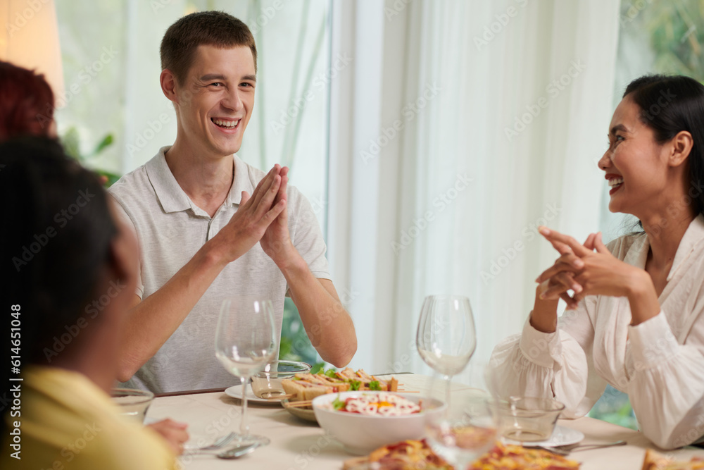 Joyful young people laughing at jokes at dinner table Joyful young people laughing at jokes at dinner table