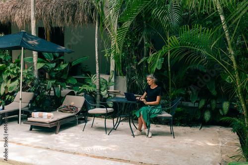 Remote work in tropic country. Woman working with laptop wjile sit in cafe with jungle view, coconut palms around photo