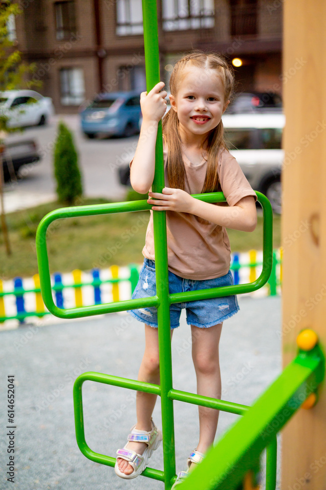a child girl on a children's multi-colored playground in the courtyard of a multi-storey house in the summer has fun playing and climbing high up the stairs, summer holidays a child girl on a children's multi-colored playground in the courtyard of a multi-storey house in the summer has fun playing and climbing high up the stairs, summer holidays