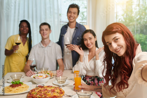 Positive red hair young woman photographing with friends at dinner party