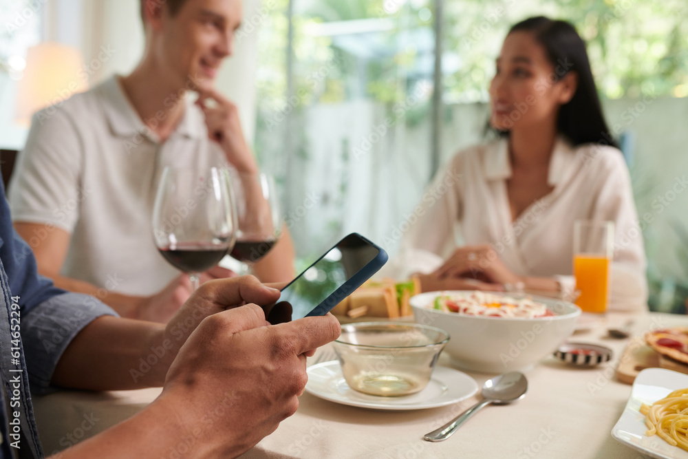 Hands of young man texting at dinner party with friends