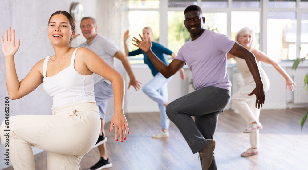Fototapeta premium Young woman coach rehearsing with group of multinational sports aged people hip hop dance in dance hall