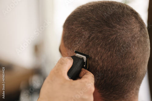Close-up of human hand hold trimmer and make hairstyle for man. Barbershop 