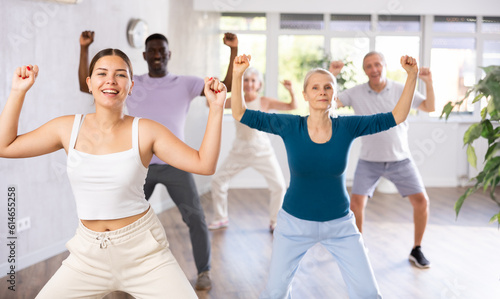 Young woman coach rehearsing with group of multinational sports aged people hip hop dance in dance hall