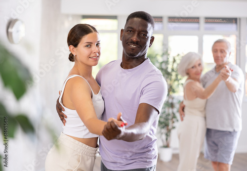 Dynamic young and mature attendees of dancing courses training poses of Waltz in dance hall