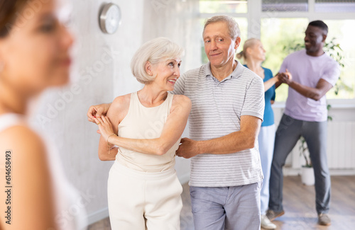 Happy smiling elderly woman enjoying impassioned merengue with male partner in latin dance class. Social dancing concept