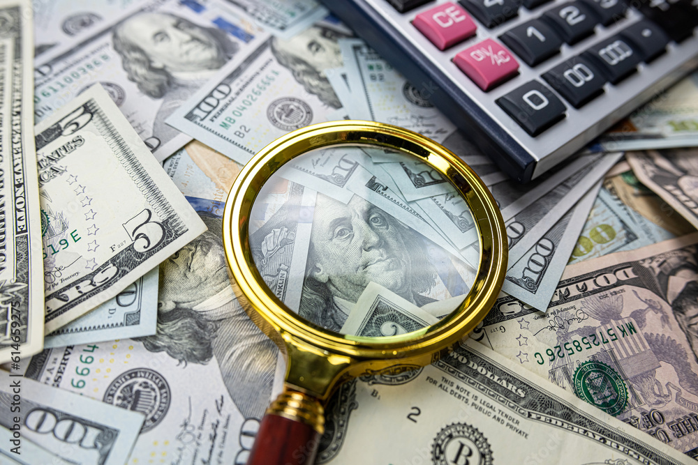 Magnifying glass with calculator over US dollar bill Magnifying glass with calculator over US dollar bill