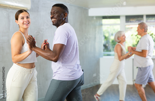 Happy attractive young girl enjoying impassioned merengue with experienced African American partner in latin dance class. Social dancing concept