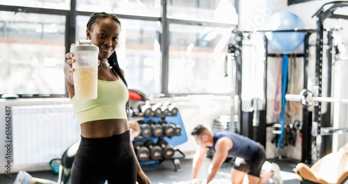 Cheerful black sportswoman with healthy protein drink in gym