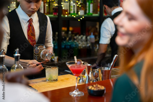 Professional male bartender preparing and serving cocktail drink to customer on bar counter at luxury nightclub. Barman making mixed alcoholic drink for celebrating holiday party at restaurant bar.