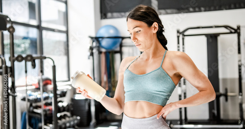 Slim woman looking at bottle of protein cocktail in gym