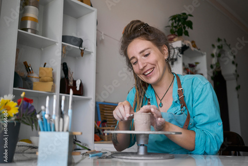 Happy woman sculpting clay cup at workshop