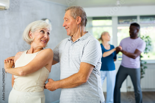 Dynamic mature attendees of dancing courses training poses of Waltz in dance hall