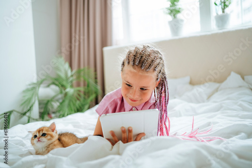 Girl holding tablet PC lying by ginger kitten on bed photo