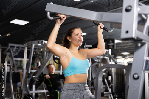 Fit young woman working out at shoulder press machine in gym