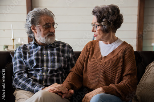 An elderly couple chatting on the sofa in a living room. Old woman in glasses posing at home indoors, lonely senior pensioner woman sitting in living room portrait