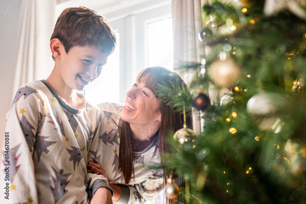 Happy mother with son standing in front of Christmas tree at home Happy mother with son standing in front of Christmas tree at home