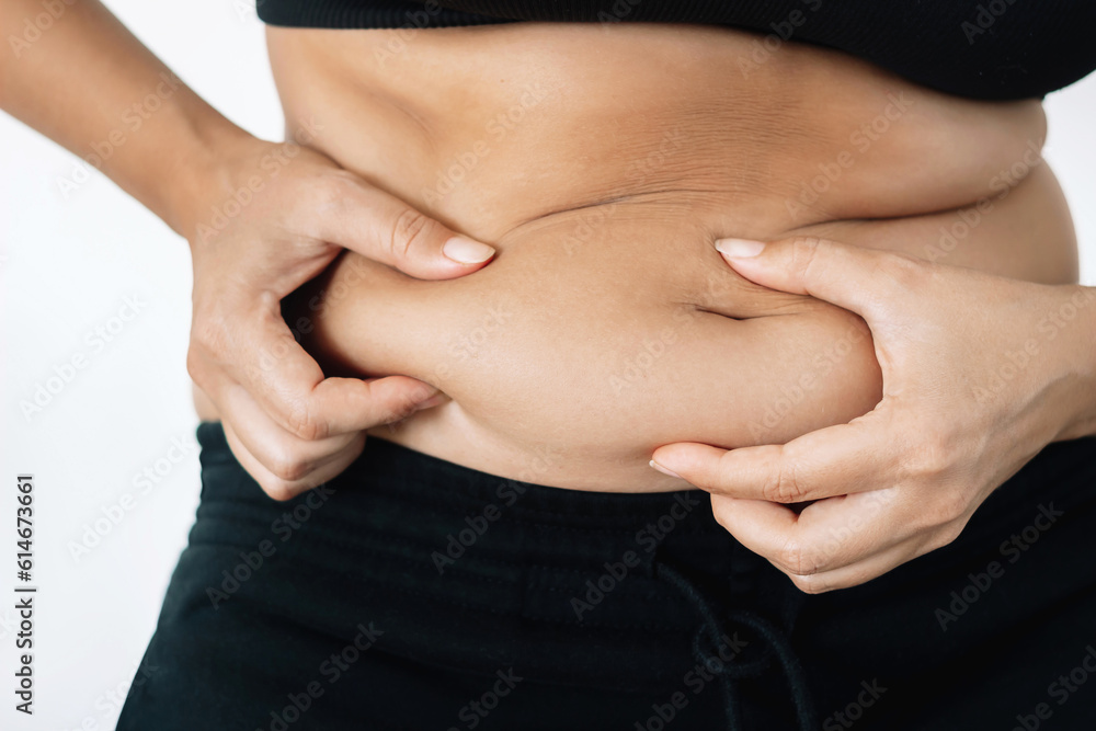 A cropped shot of a young woman in a black underwear holding herself by the fat on her stomach isolated on a white background. Overeating, overweight, excess weight, hormonal belly, rolls A cropped shot of a young woman in a black underwear holding herself by the fat on her stomach isolated on a white background. Overeating, overweight, excess weight, hormonal belly, rolls