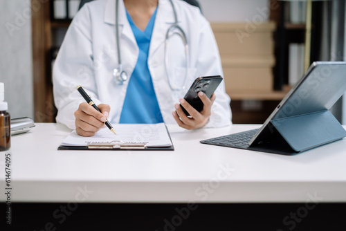 Physician or practitioner in room writing on blank notebook and work on laptop computer  smartphone on the desk   Medic tech concept.