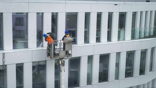 Two workers wearing safety harness wash office building facade at
