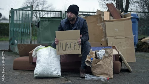 Poorly and dirtyly dressed man sits by a pile of rubbish and holds a poster HUNGRAY in his hands. photo
