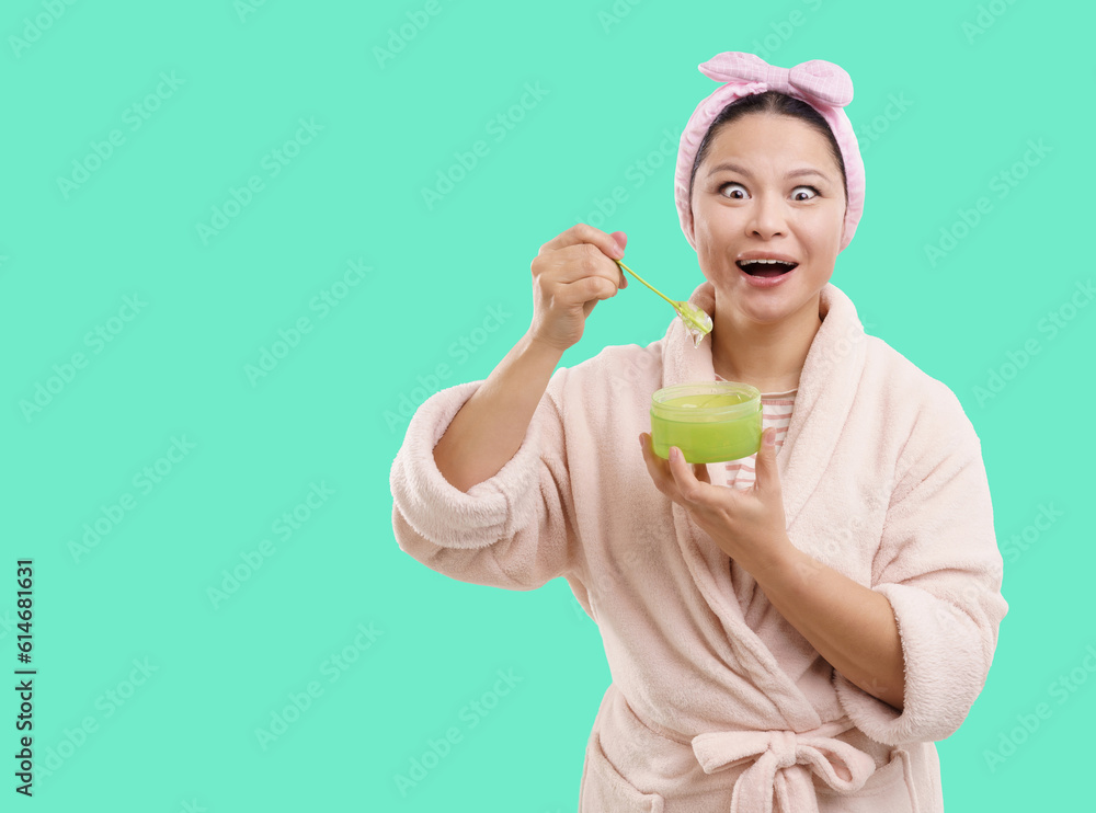 Excited Asian woman wearing bathrobe smiles at camera while opening cosmetic jar containing transparent cream. Isolated on vibrant green background, creating fresh and captivating visual. . High Excited Asian woman wearing bathrobe smiles at camera while opening cosmetic jar containing transparent cream. Isolated on vibrant green background, creating fresh and captivating visual. . High