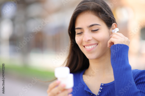 Happy woman putting earbud in the street