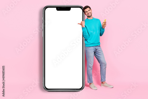 Full body photo of handsome young guy beaming smile hold gadget finger point banner wear trendy blue look isolated on pink color background