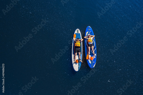 Fototapeta Funny man and woman floats on supboard on lake, top view from drone