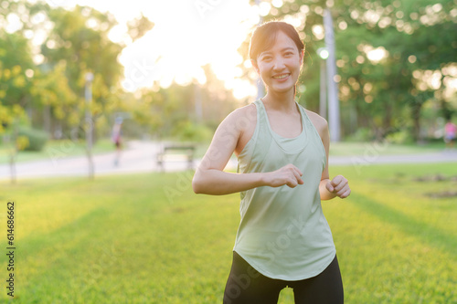 Fototapeta Naklejka Na Ścianę i Meble -  Female jogger. Fit young Asian woman with green sportswear stretching muscle in park before running and enjoying a healthy outdoor. Fitness runner girl in public park. Wellness being concept
