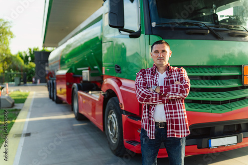a male tanker or truck driver poses next to his vehicle at a gas station, casually dressed and ready to go