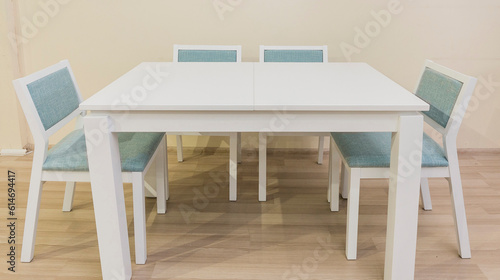 A white table with four legs and four chairs stands in the room