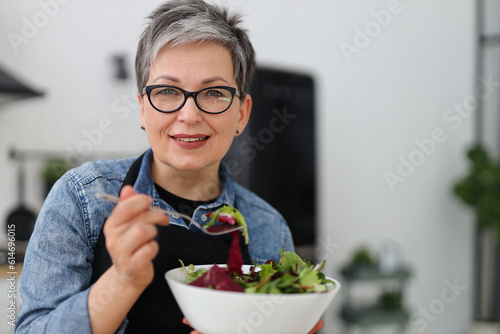 Smiling senior woman in glasses holding a plate of vegetable salad.