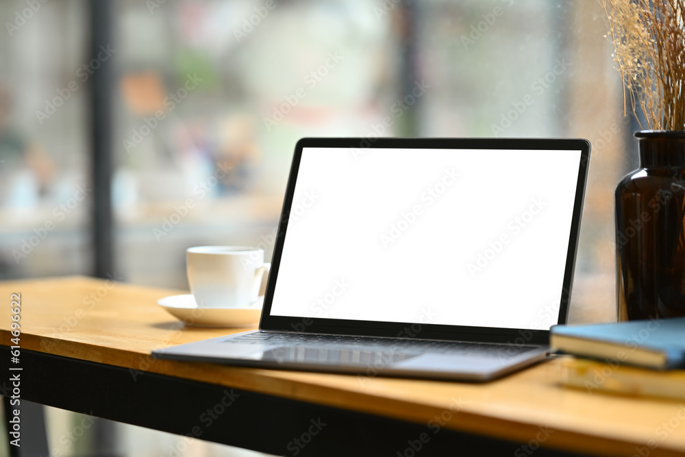 Wooden office desk with laptop computer, notepad, and cup of coffee. White blank screen for your advertising text Wooden office desk with laptop computer, notepad, and cup of coffee. White blank screen for your advertising text
