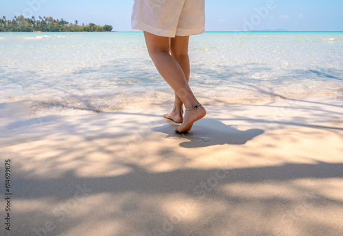 Walking on the beach. Barefoot woman in white pants walk on bright clean sandy seashore in the warm sunlight at the Koh Kood island in Thailand. Summer traveling alone and holiday vacation concepts.
