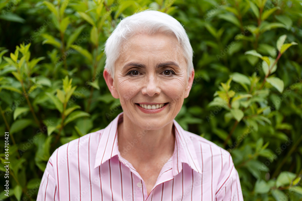 Closeup portrait of smiling senior woman looking at camera in green park. Confident gray haired businesswoman posing for picture outdoors Closeup portrait of smiling senior woman looking at camera in green park. Confident gray haired businesswoman posing for picture outdoors
