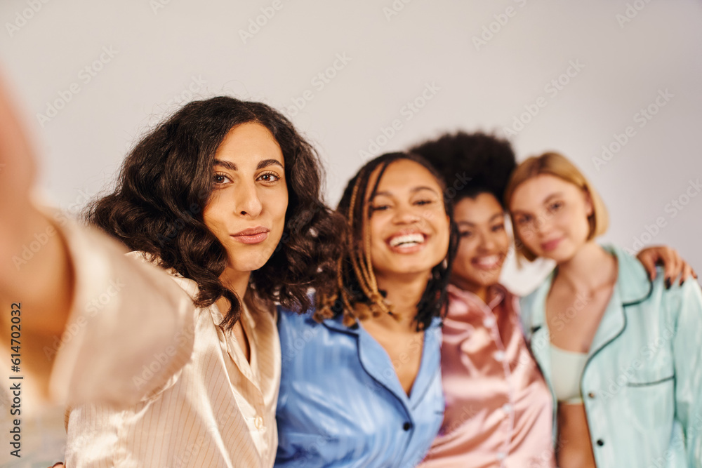 Multiracial woman in pajama looking at camera while standing near cheerful and blurred multiethnic girlfriends at home during slumber party, bonding time in comfortable sleepwear Multiracial woman in pajama looking at camera while standing near cheerful and blurred multiethnic girlfriends at home during slumber party, bonding time in comfortable sleepwear